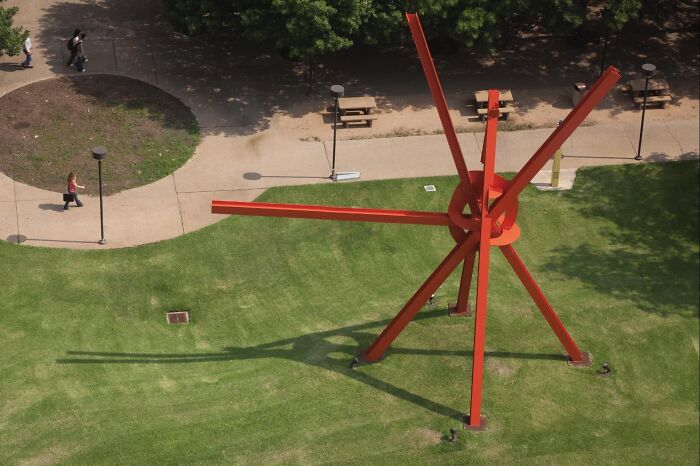 An abstract red steel structure on a grassy lawn, representing examples of public art