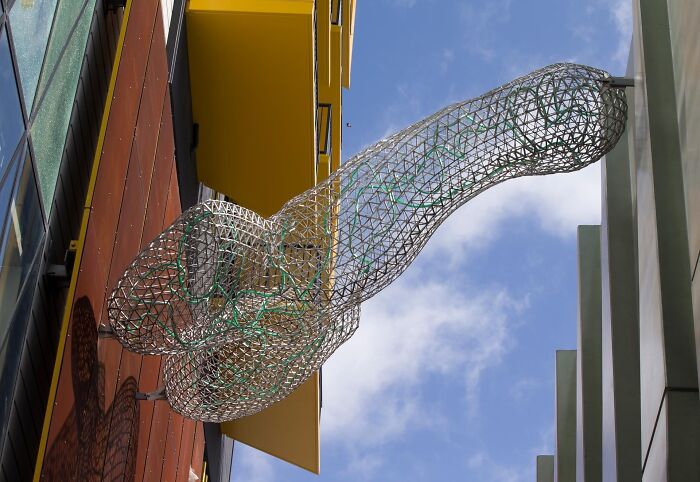A wireframe phallic sculpture attached to a building, showing bizarre public art.