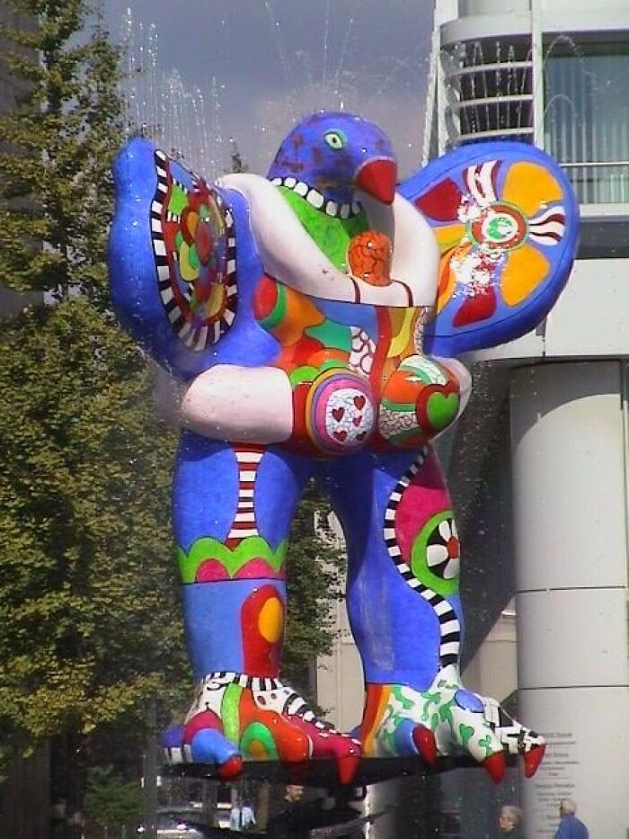 A colorful, bizarre bird statue in a fountain representing a strange example of public art.