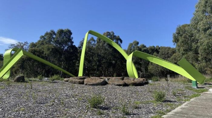 A large abstract green ribbon structure representing modern public art in an outdoor park