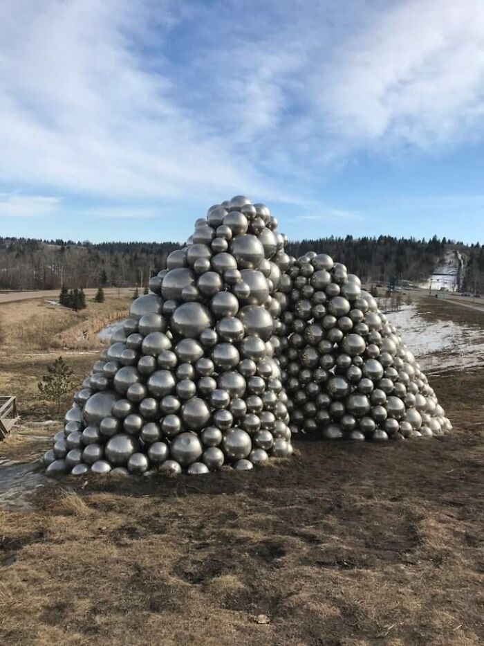 A large pile of metallic silver spheres forming two mounds in an open field, showcasing outdoor public art.