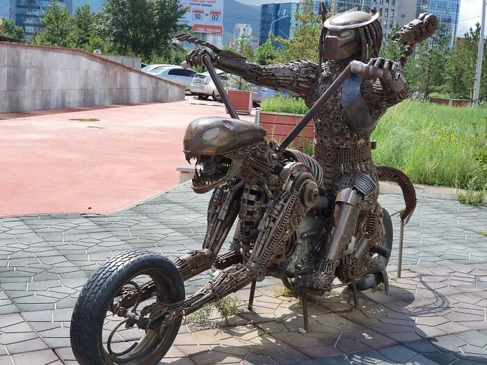 A metal sculpture of Predator riding an Alien-themed motorcycle, showing unique public art
