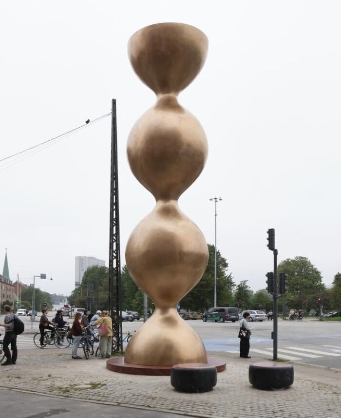 A tall, bulbous golden tower sculpture on a city street, demonstrating examples of public art.
