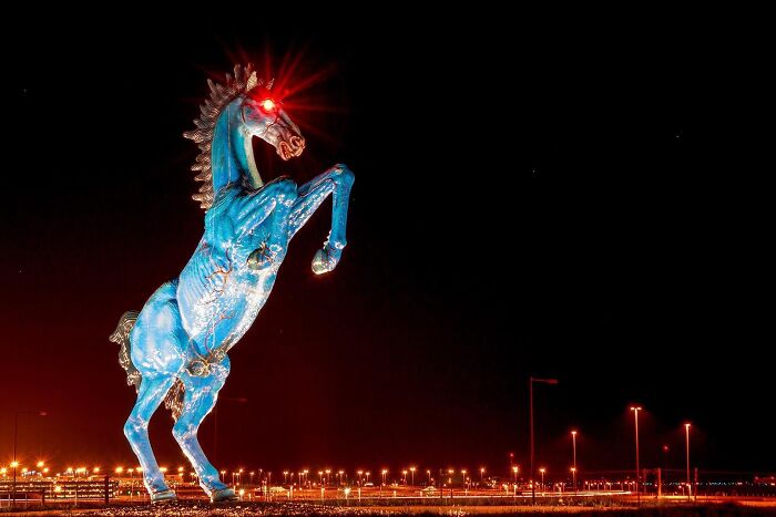 A towering blue horse statue with glowing red eyes, showing a dramatic example of public art.