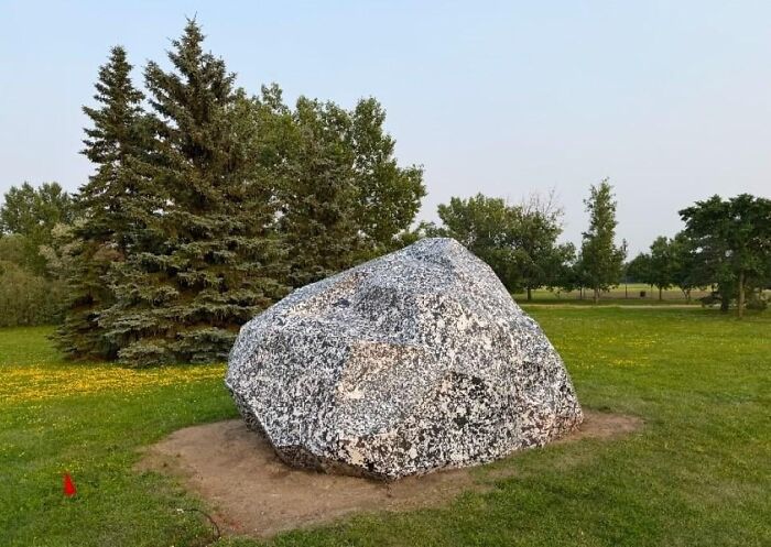 A massive public art installation of a boulder painted with black and white speckled patterns on grass.