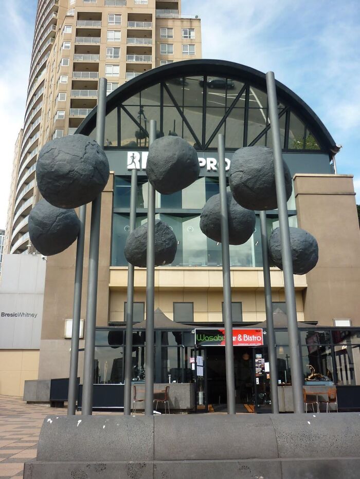 Public art installation featuring large grey boulder-like structures mounted high on metal poles.