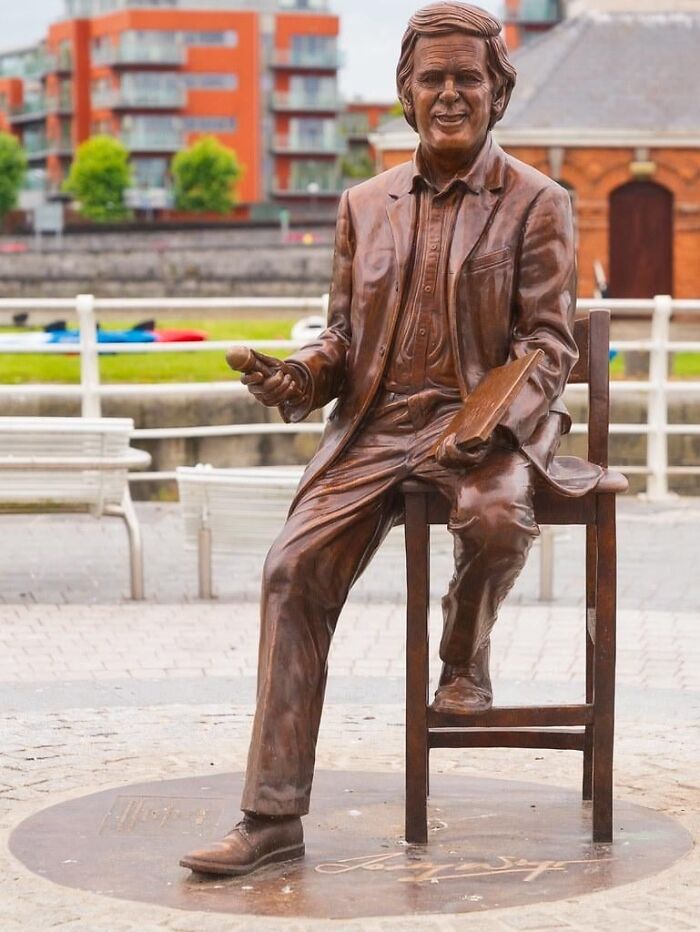 A bronze statue of a smiling man sitting on a stool, showing a bad example of public art