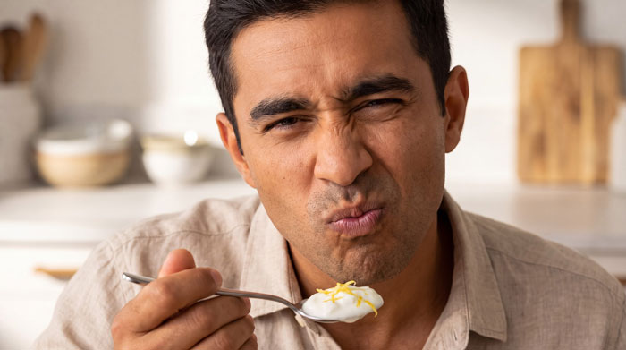 Man showing a disgust expression while eating, illustrating dislike for wife's cultural cuisine. Man showing a disgust expression while eating, illustrating dislike for wife's cultural cuisine.
