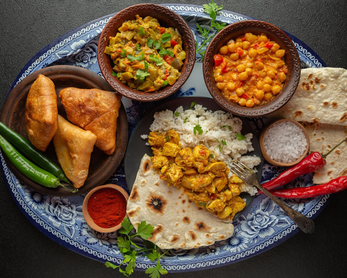 An assortment of traditional cultural cuisine served on a decorated platter with curry, rice, and samosas. An assortment of traditional cultural cuisine served on a decorated platter with curry, rice, and samosas.