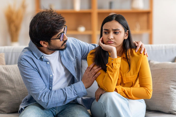 Man attempting to comfort his upset wife on the couch, reflecting a changing relationship dynamic. Man attempting to comfort his upset wife on the couch, reflecting a changing relationship dynamic.