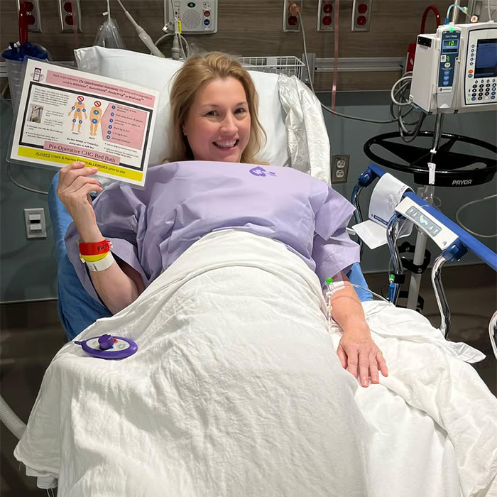 A smiling woman in a hospital bed holding medical instructions, facing health challenges from cancer diagnoses.