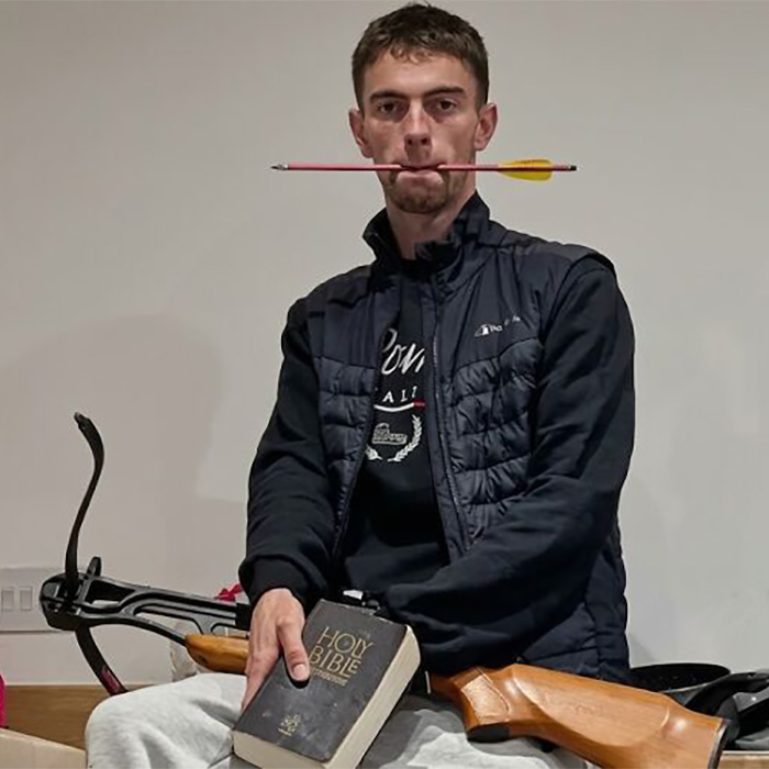 Man holding Bible and wooden rifle with arrow in mouth Man holding Bible and wooden rifle with arrow in mouth