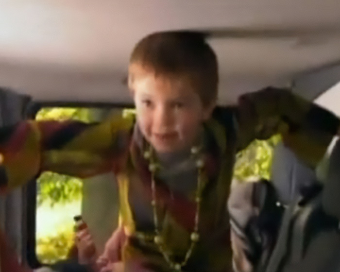 Young boy climbing inside vehicle wearing colorful shirt and necklace Young boy climbing inside vehicle wearing colorful shirt and necklace