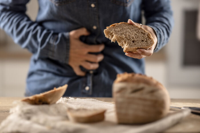 A woman holding a slice of bread with a hand on her stomach, representing health problems.