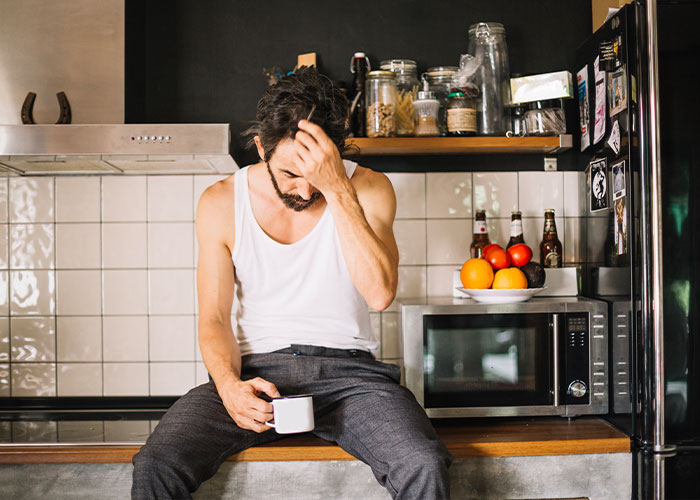 Distressed man holding a coffee cup while sitting on a kitchen counter, contemplating a fiancé’s lie. Distressed man holding a coffee cup while sitting on a kitchen counter, contemplating a fiancé’s lie.