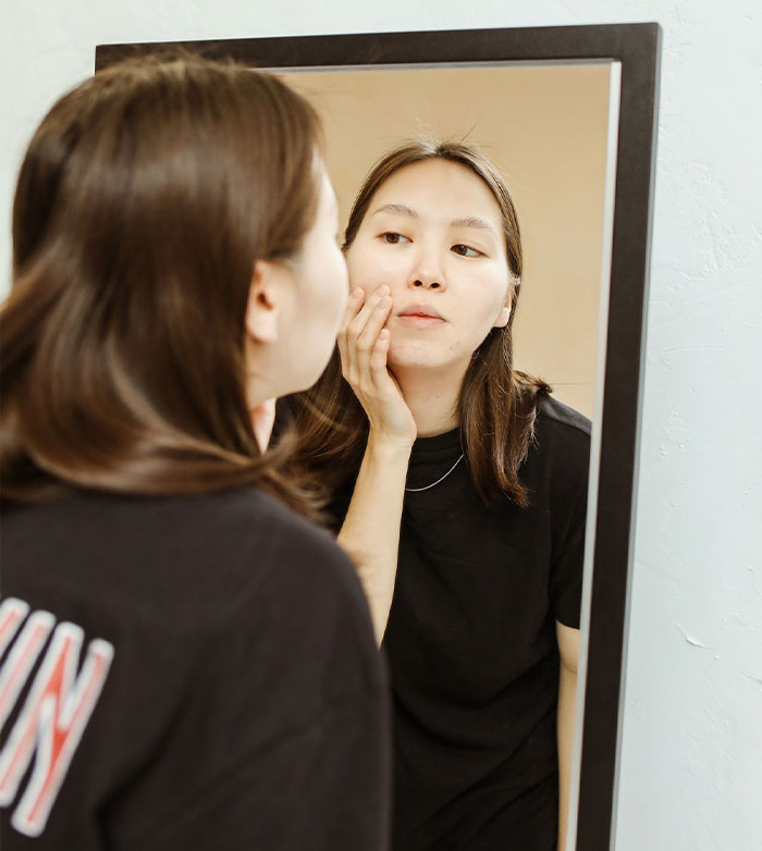 Woman examining her skin in the mirror after a cosmetic injection procedure Woman examining her skin in the mirror after a cosmetic injection procedure