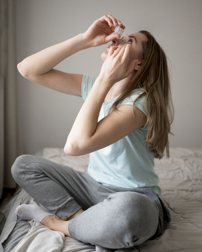 Young woman applying eye drops while sitting on a bed, addressing common Gen Z health problems.