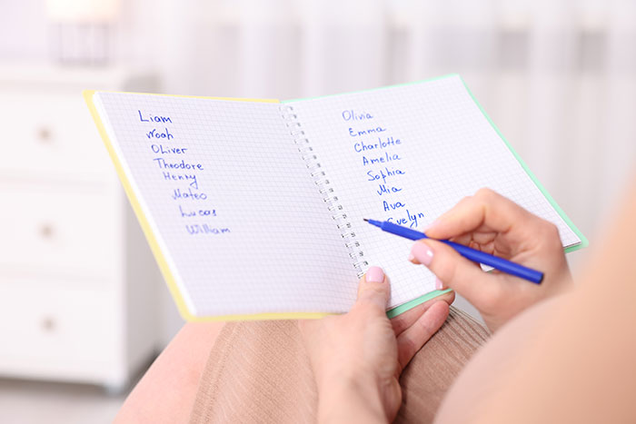A person writing down baby name ideas in a notebook, including names like Lucifer.