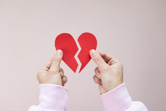 Hands holding two halves of a torn red paper heart, symbolizing people behaving like the world owed them everything