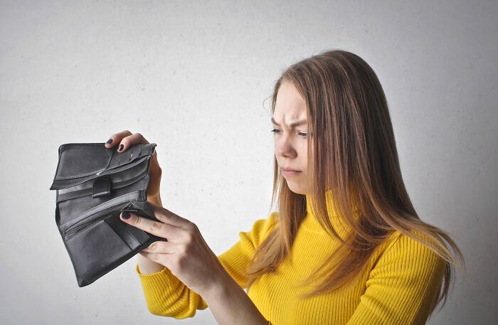 Disappointed woman looking at her empty black wallet, showing how people behaving like the world owed them everything