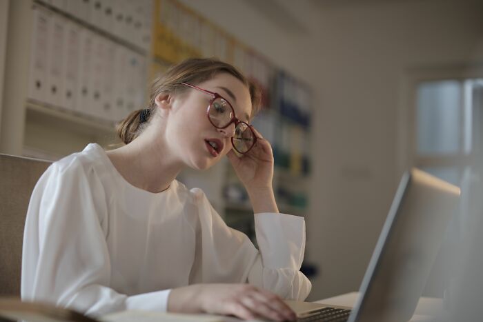 A stressed woman looks at her laptop, showing people behaving like they are owed everything in the office