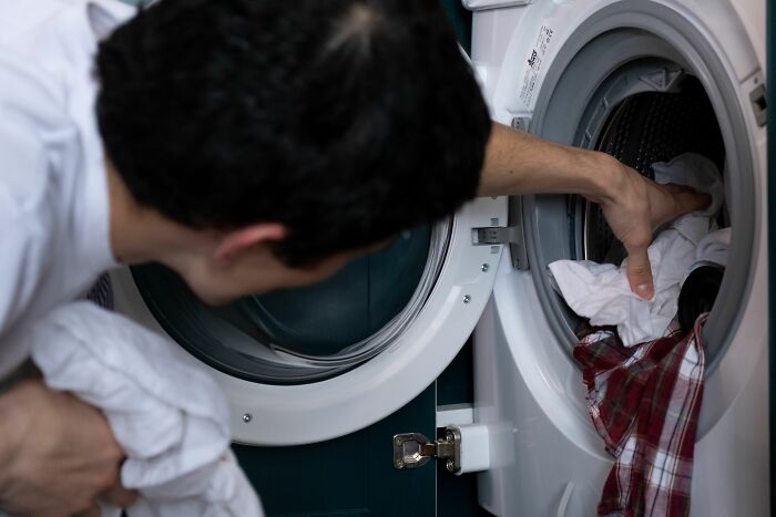Man loading white laundry into a washing machine, illustrating people behaving like the world owed them everything