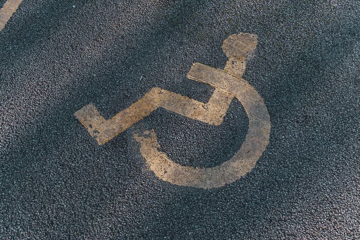 An old disabled parking symbol painted on asphalt, showing people behaving like they are owed everything