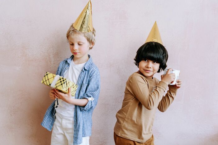 Two kids in party hats with gifts, showing how some people grow up behaving like the world owed them everything.