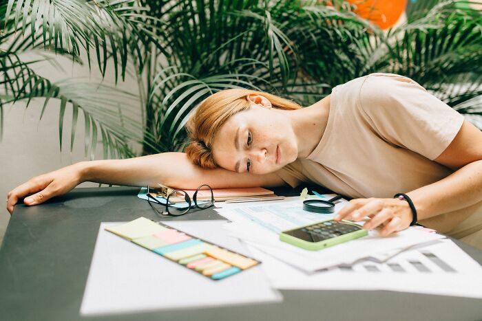 Exhausted woman resting her head on a desk with paperwork and a calculator, behaving like the world owed them everything
