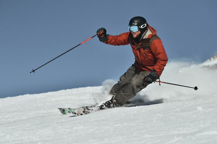 A skier in an orange jacket sliding down a snowy slope, representing stories of people behaving like they own the world
