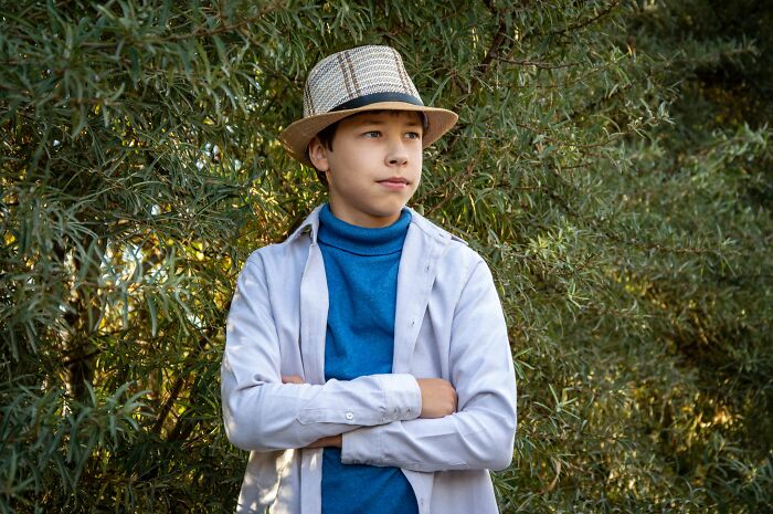 A young boy wearing a fedora hat and a blue turtleneck with crossed arms, symbolizing people behaving with entitlement