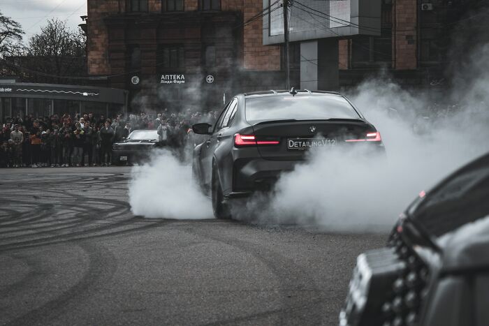 Black car performing a burnout with smoke in a street crowd scene for BF phone shock