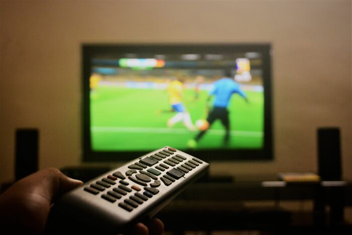 Hand holding remote control toward TV showing soccer match