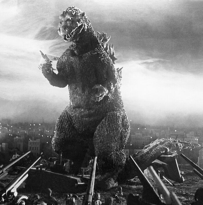 Black and white image of Godzilla surrounded by guns in a city scene