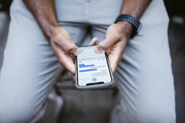 Person texting on their phone holding it with both hands sitting down
