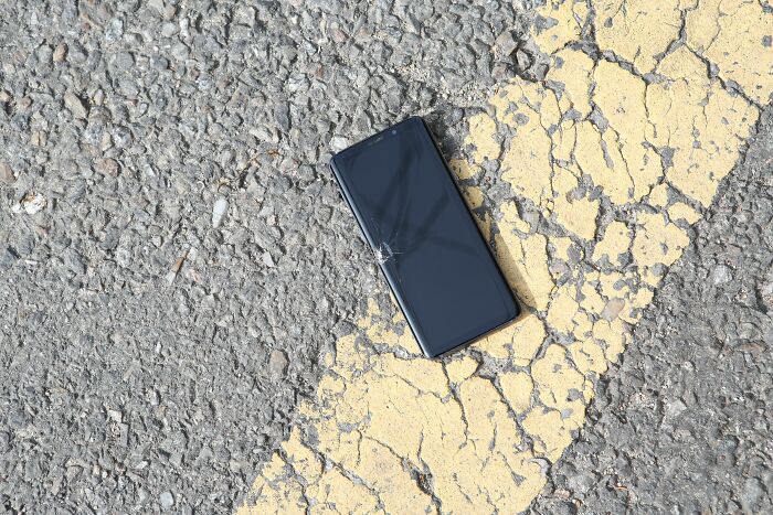 Broken phone with cracked screen lying on cracked asphalt near yellow line