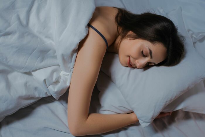 Woman peacefully sleeping in bed with white sheets