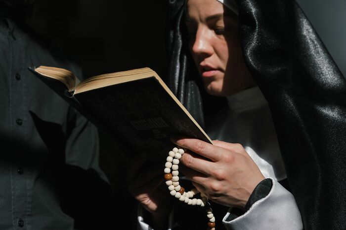 Nun holding a book and rosary beads in a focused religious moment