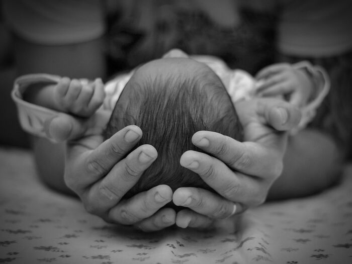 Black and white image of hands cradling a newborn baby's head
