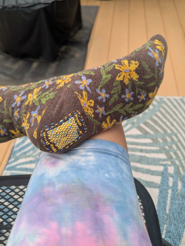 A floral sock repaired with yellow stitching, showing how creativity can save money through visible mending