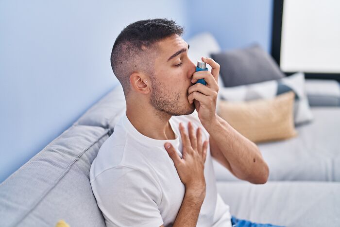 A young man using an inhaler on a couch, showing respiratory health problems in Gen Z.