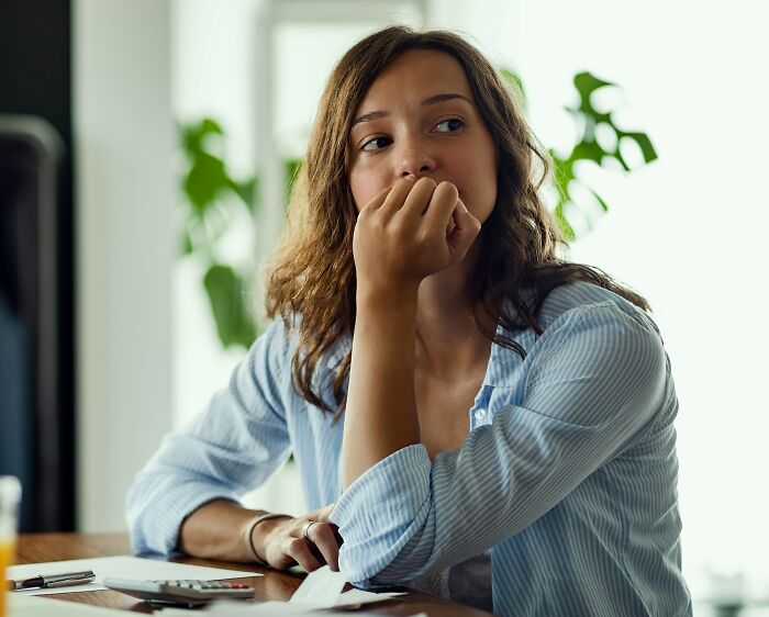 A pensive young woman sitting at a table, contemplating things women wish they knew