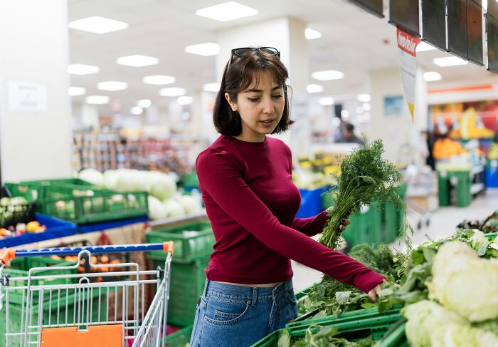 A woman choosing fresh herbs at a grocery store, representing daily life with partners.