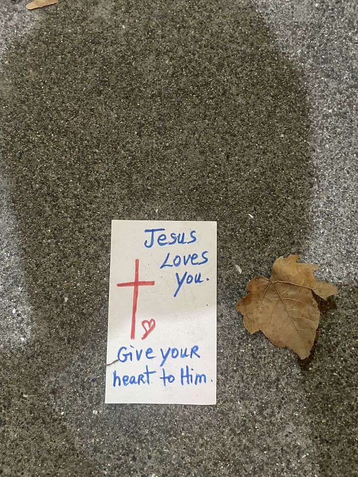Religious handwritten note with a cross lying outdoors on pavement next to a leaf as found paper